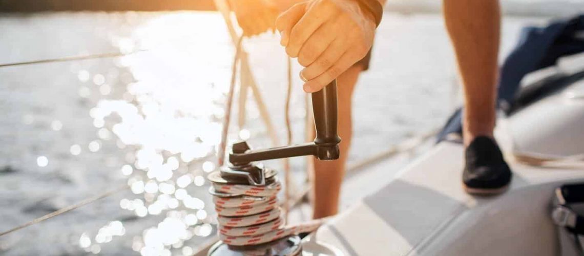 close-up-sailor-winds-around-rope-by-using-handle-coiling-he-works-with-both-hands-young-man-stands-yacht
